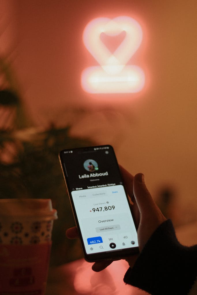 Smartphone display with neon heart backdrop, showcasing modern technology in a cozy setting.